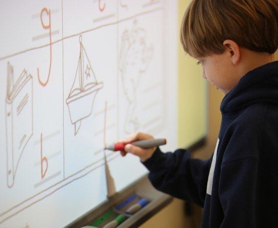 A young student practices writing on a smart board