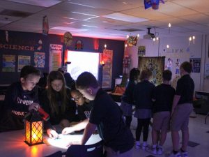 Working by lamplight, students in STEM class escape room look for clues.