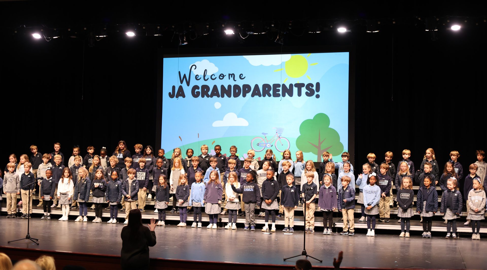 First grade students sing to their grandparents from the Performing Arts stage/
