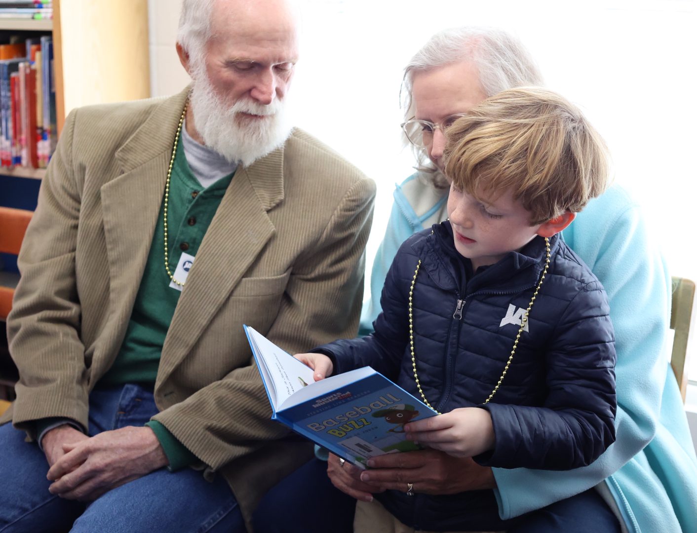A grandfather and grandmother read with their grandchild at school.
