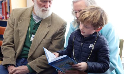 A grandfather and grandmother read with their grandchild at school.